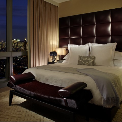 a bed with a leather headboard and a bench in a room with a city view