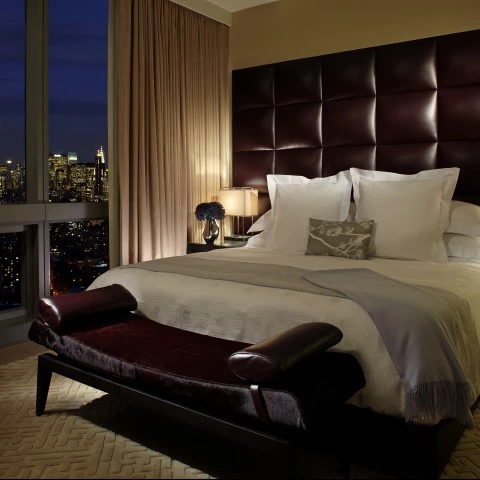 a bed with a leather headboard and a bench in a room with a city view