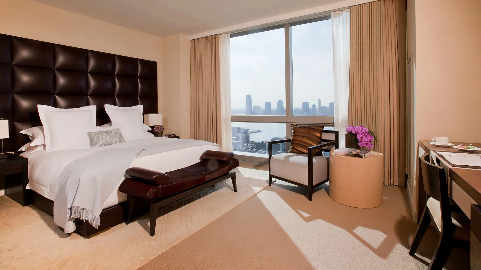 A hotel room with a large bed, desk, chair, and city view.