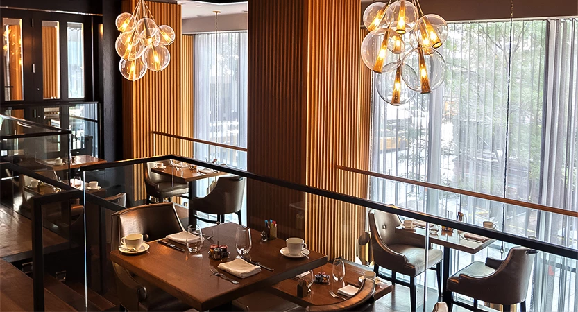 A dining area with tables and chairs, glass railing, and large windows.