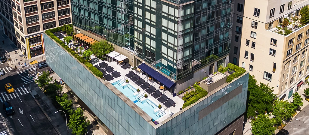 Aerial view of a rooftop pool with lounge chairs and umbrellas on a building in New York City