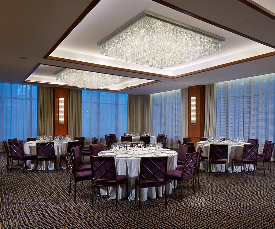 A large meeting room with round tables, purple chairs, and chandeliers.