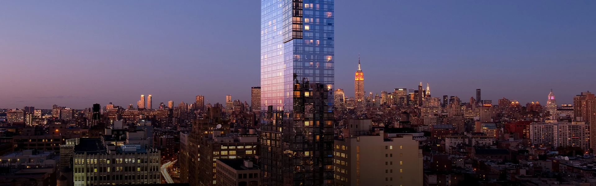 A cityscape at dusk with a prominent skyscraper in the center