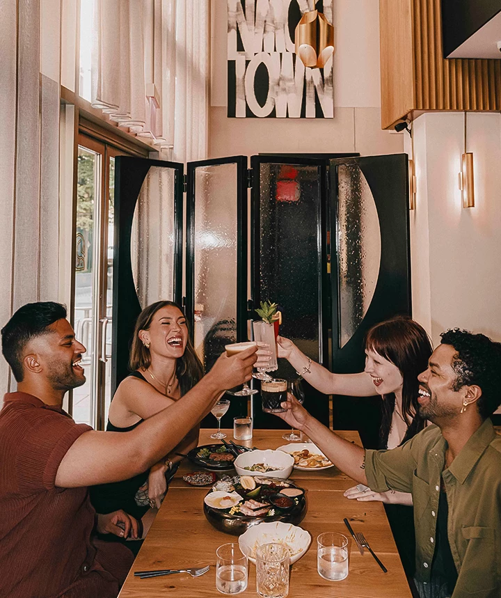 A group of four people cheering and having a meal together at a restaurant.