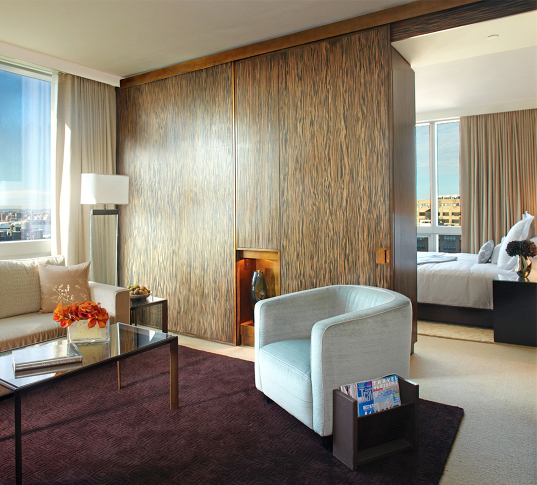 A wide view of a hotel room with a sofa, chair, coffee table, and a bed in the background.