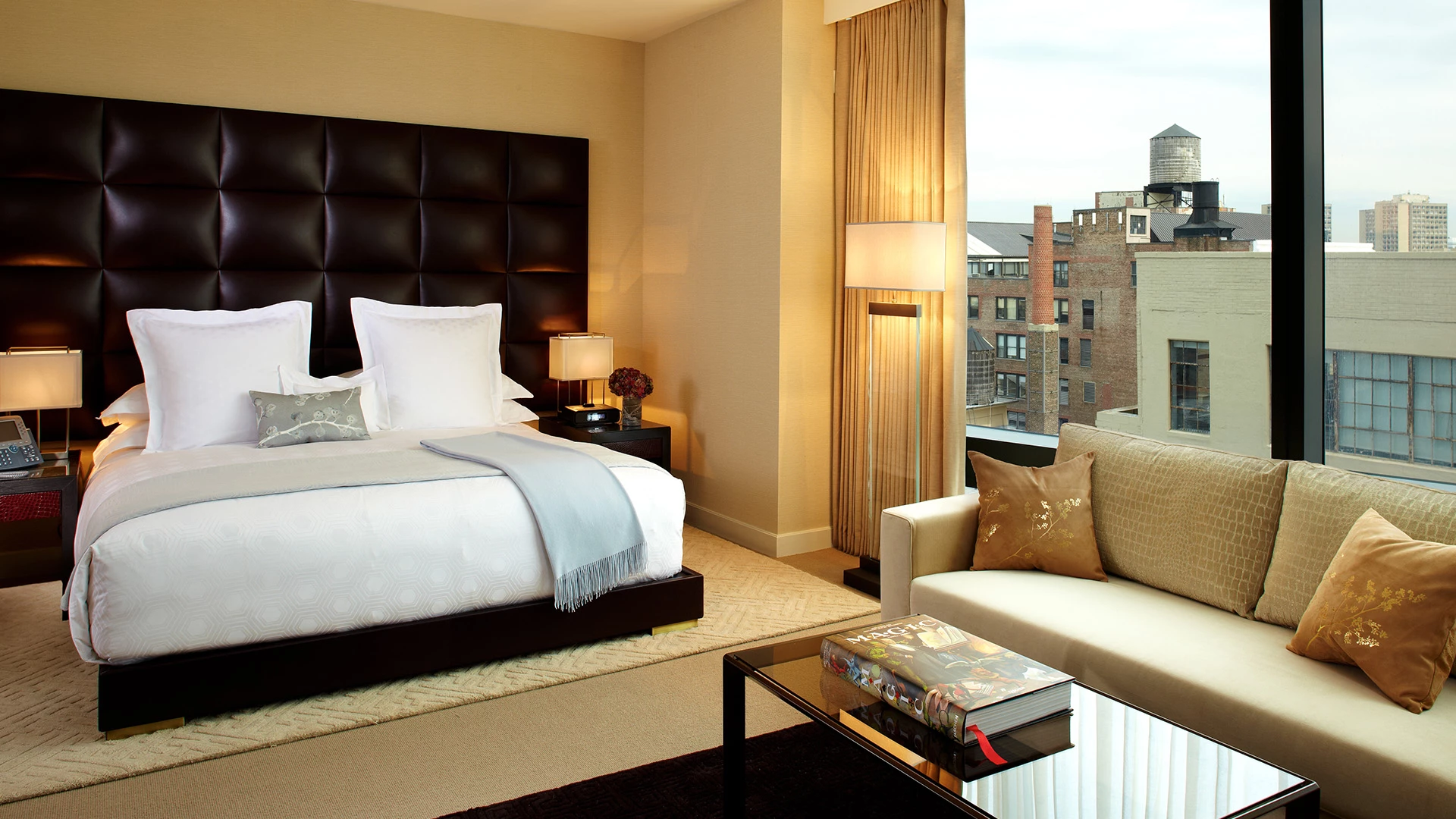 A luxurious hotel room with a large bed, sofa, and city view.