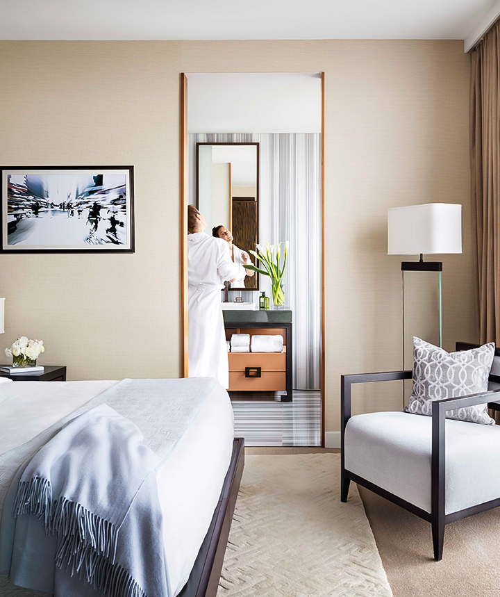 A hotel room with a bed, chair, lamp, and mirror