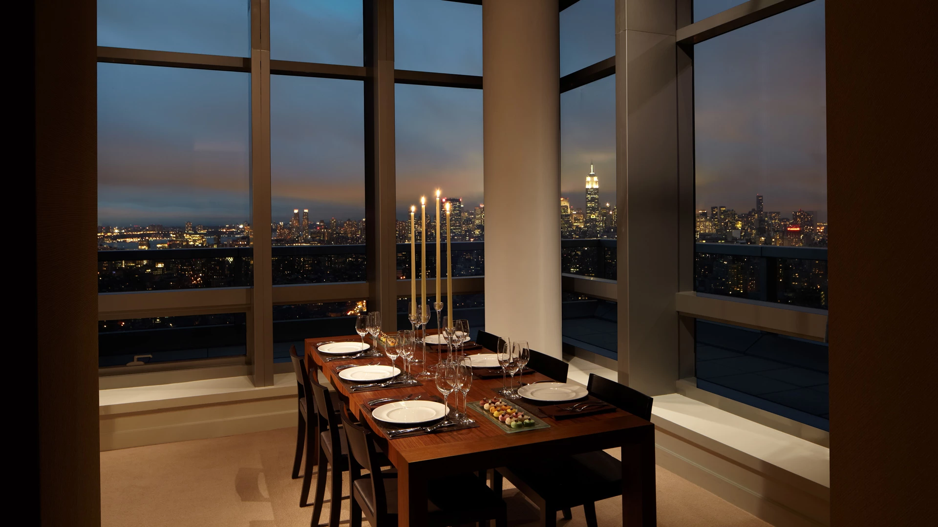 A dining table set for dinner with a city view at dusk.