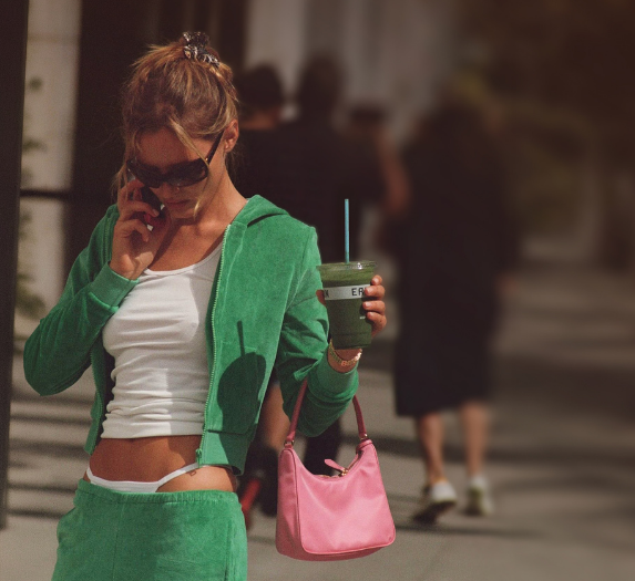 a woman in a green outfit talking on a cell phone while holding a drink