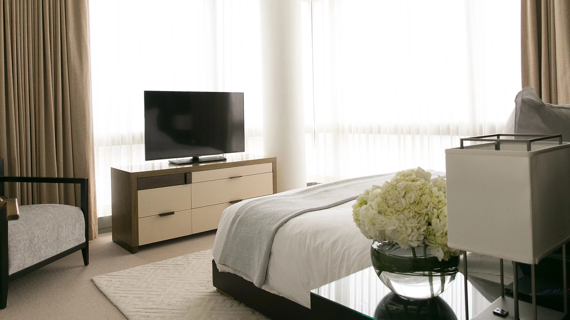A wide view of a hotel room with a bed, TV, and chair.