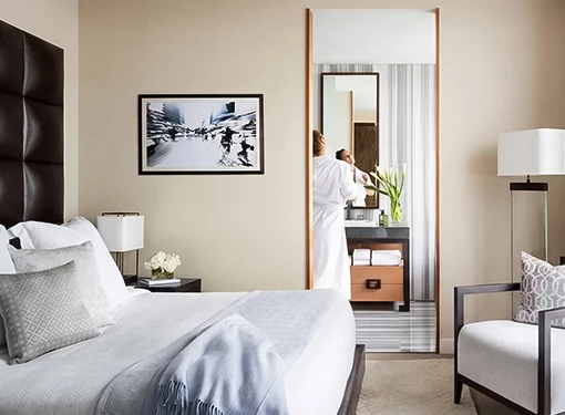 A hotel room with a bed, chair, and lamp, with a doorway leading to a bathroom.