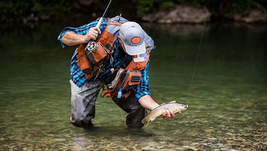 man picking up a fish from water hooked on rod