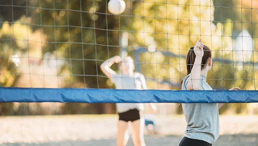 2 girls playing volleyball on sand pit court