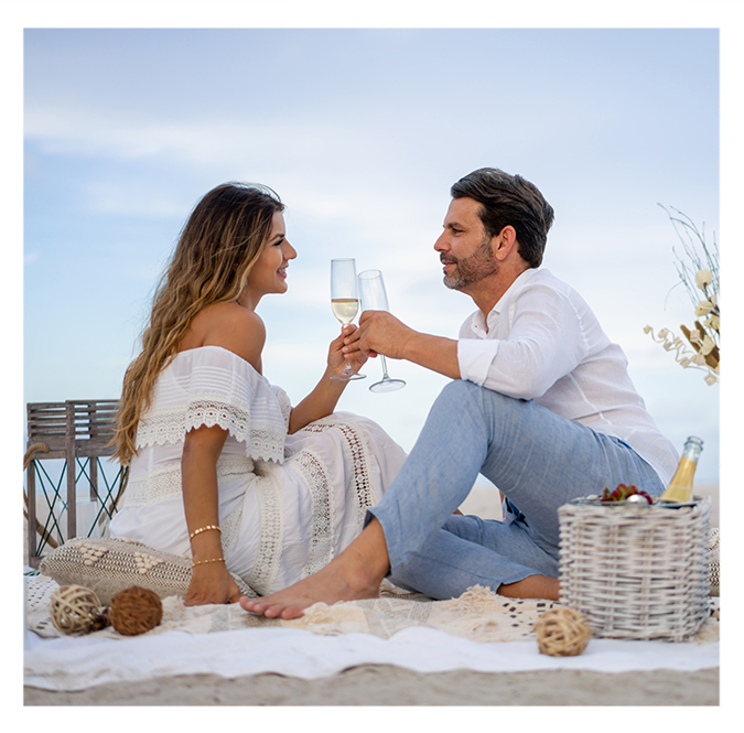 a man and woman sitting on a blanket and holding wine glasses