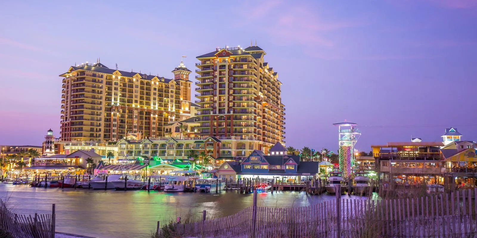 A waterfront view of a large hotel complex with boats and lights at dusk.
