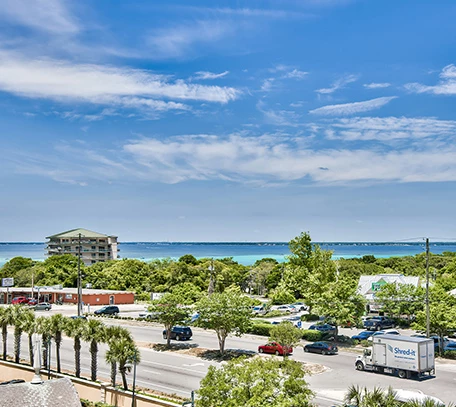 a road with cars and trees and buildings and a body of water