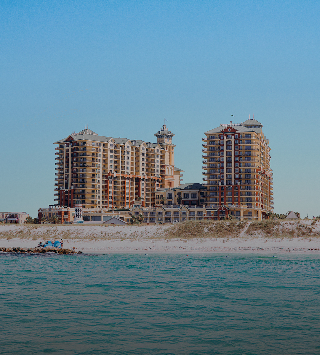 A high-rise hotel building with balconies situated on a beachfront property.