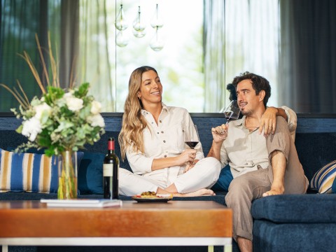 a man and woman sitting on a couch drinking wine