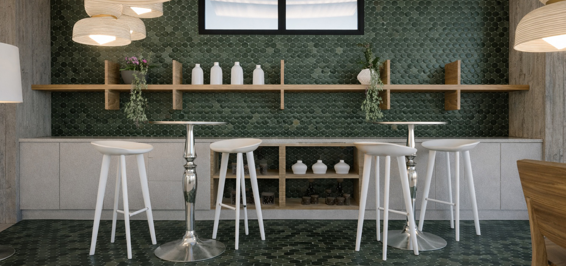 a room with a green tile wall and white stools
