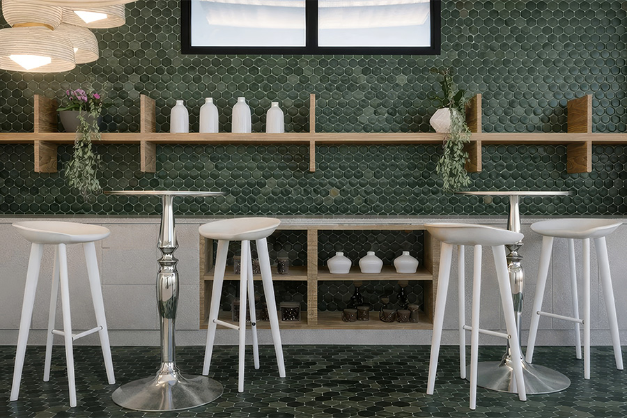 a room with a green tile wall and white stools