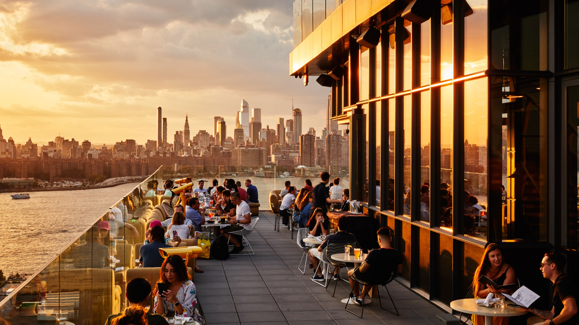 a group of people sitting at tables on a rooftop overlooking a city