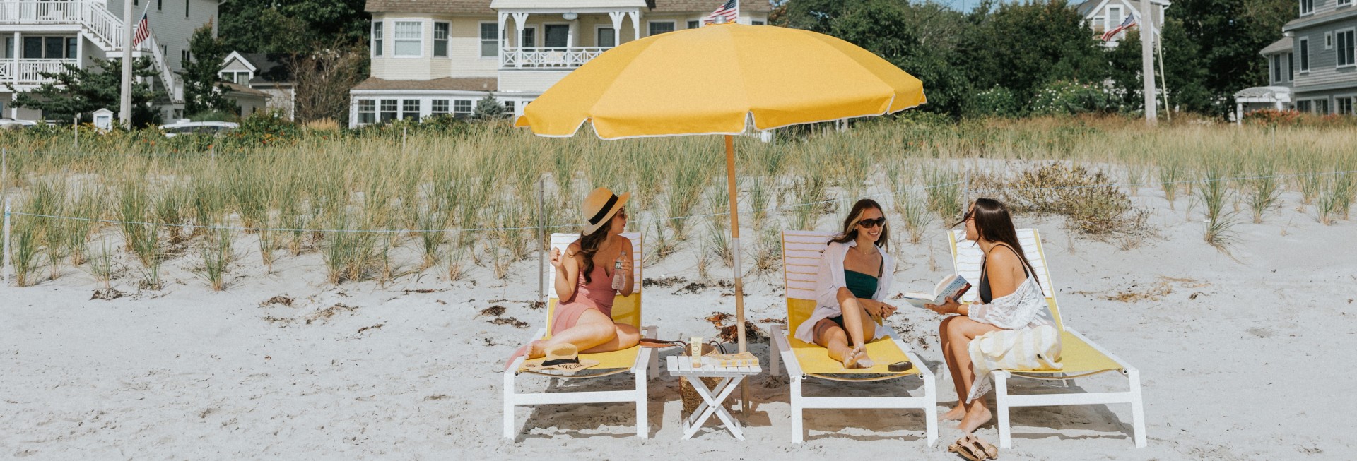 a group of women sitting under a yellow umbrella on a beach