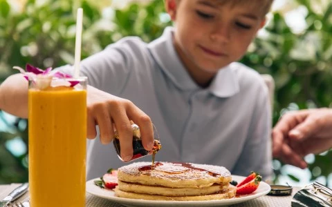 a boy pouring syrup onto a stack of pancakes