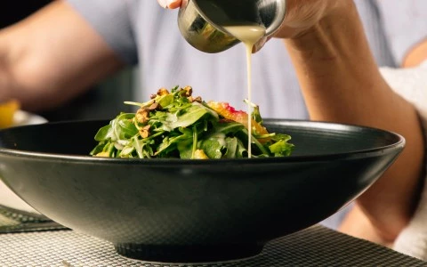 a person pouring sauce into a bowl of salad