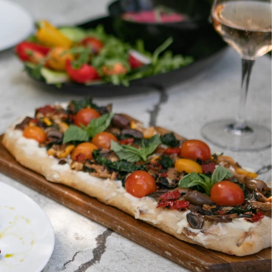 a pizza on a wooden board next to a plate of salad