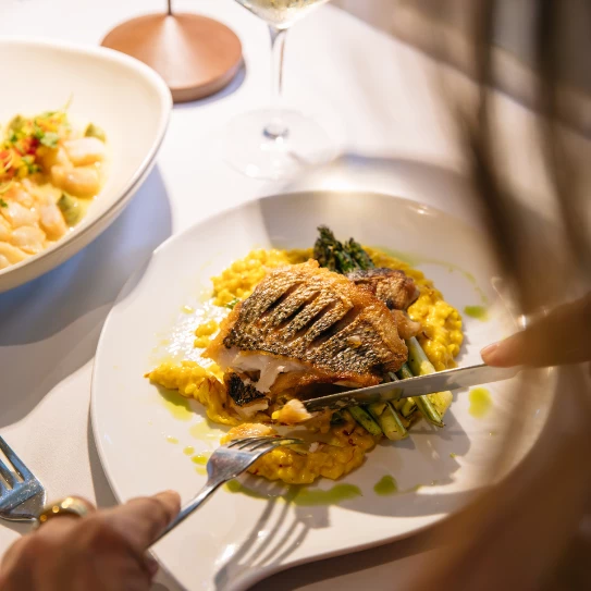 a person cutting a piece of fish on a plate with food on it