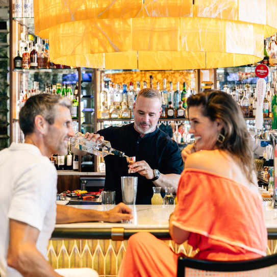 a man pouring liquid into a glass of liquid into a man at a bar