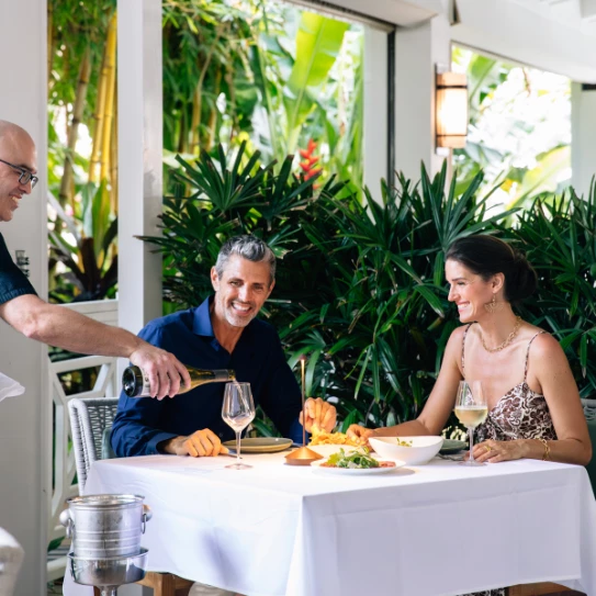 a man pouring wine into a glass to a couple of people sitting at a table