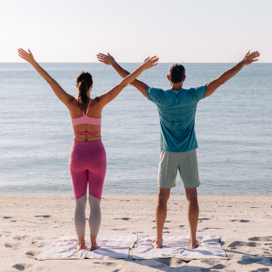 a man and woman standing on the beach with their arms up