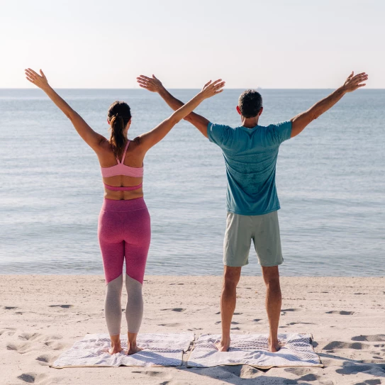 a man and woman standing on the beach with their arms up