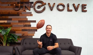 a smiling man throwing a football in the air while sitting on a couch