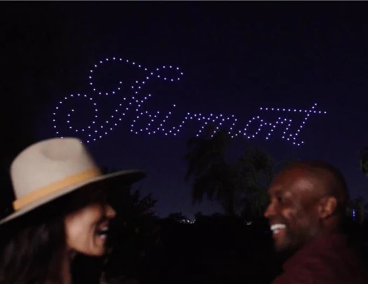 a man and woman smiling at night with drones behind them