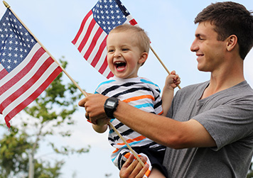 man carrying young child holding an american flags