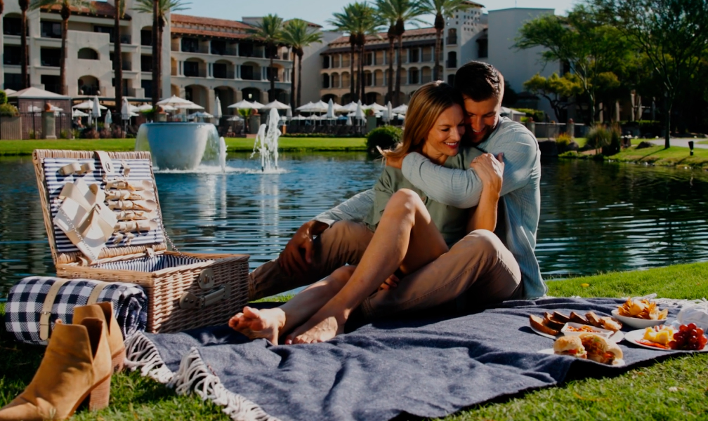 a man and woman hugging on a blanket by a pond