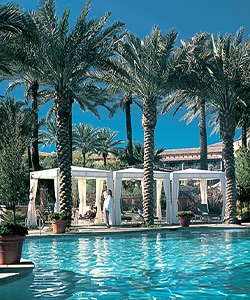 a couple of people in white robes standing next to a pool with palm trees and a building in