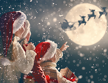 a few small kids wearing santa hats looking up and pointing to an image of santa and reindeer flying over a full moon