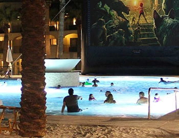 Guests watch a movie from the pool on a large outdoor screen