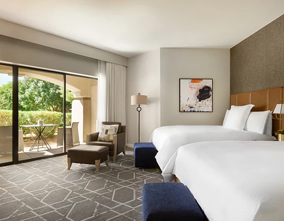 Guest room with two queen beds, arm chair and sliding glass door leading to a patio