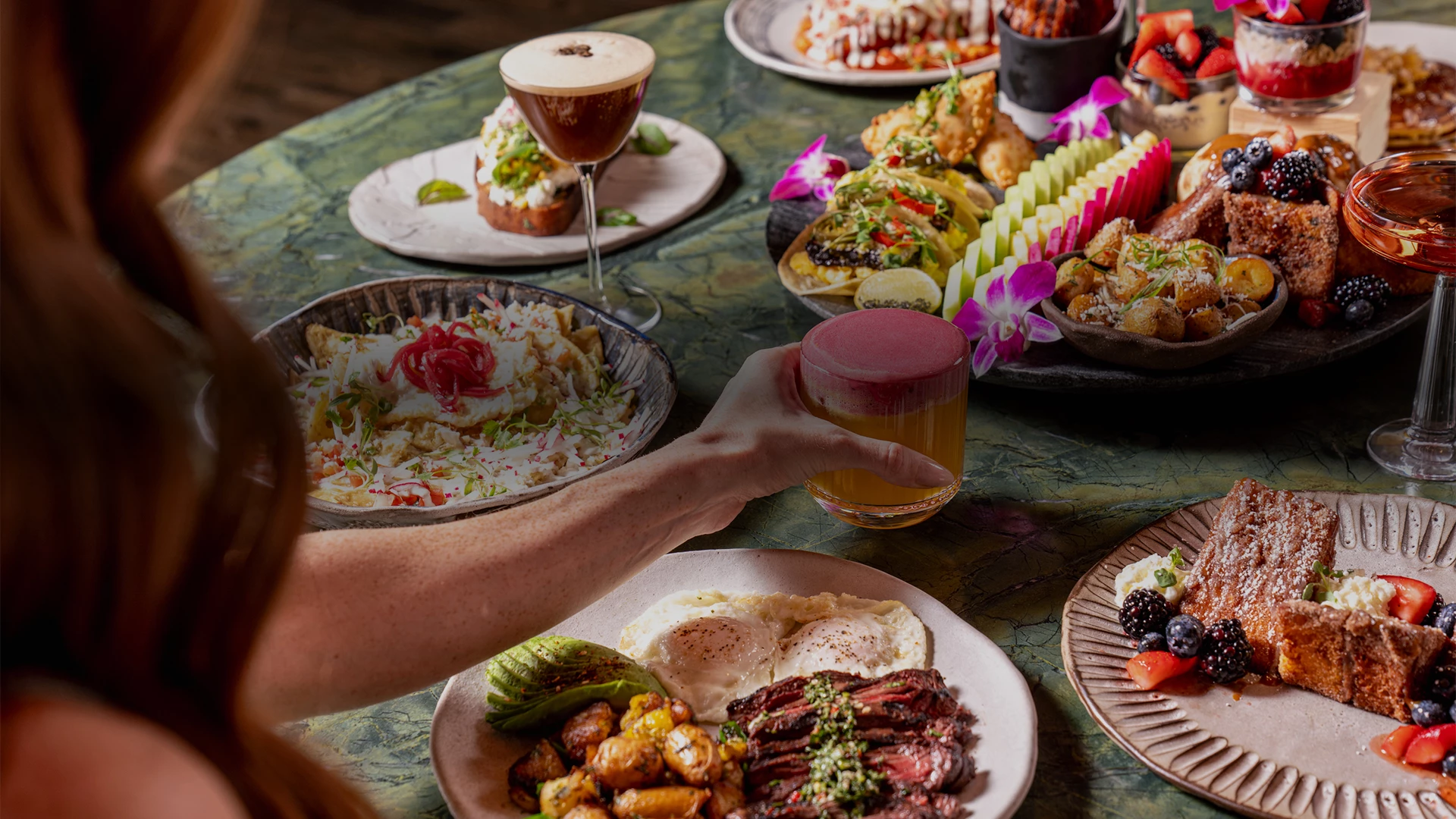 a hand holding a glass of juice over a table full of food