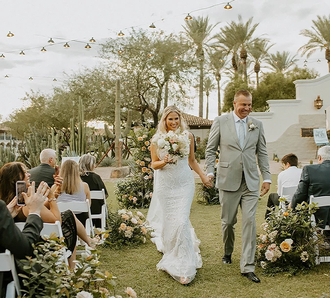 a man and woman walking down a lawn with people in the background