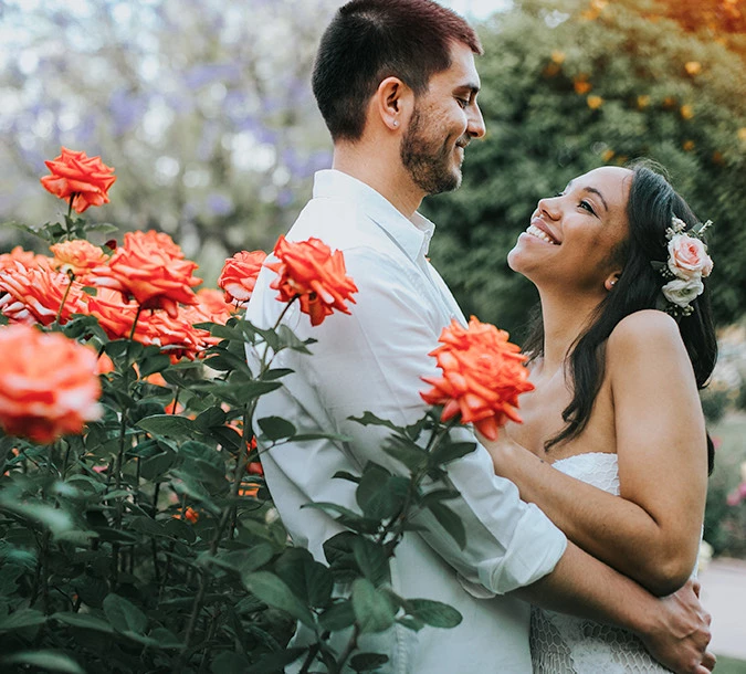 Bride and groom embracing next to orange and white roses