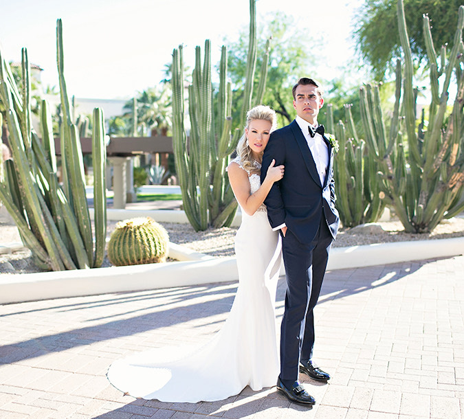 a bride and groom standing outside and looking to the right with lots of cacti behind them