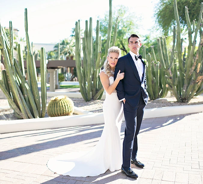 a bride and groom standing outside and looking to the right with lots of cacti behind them
