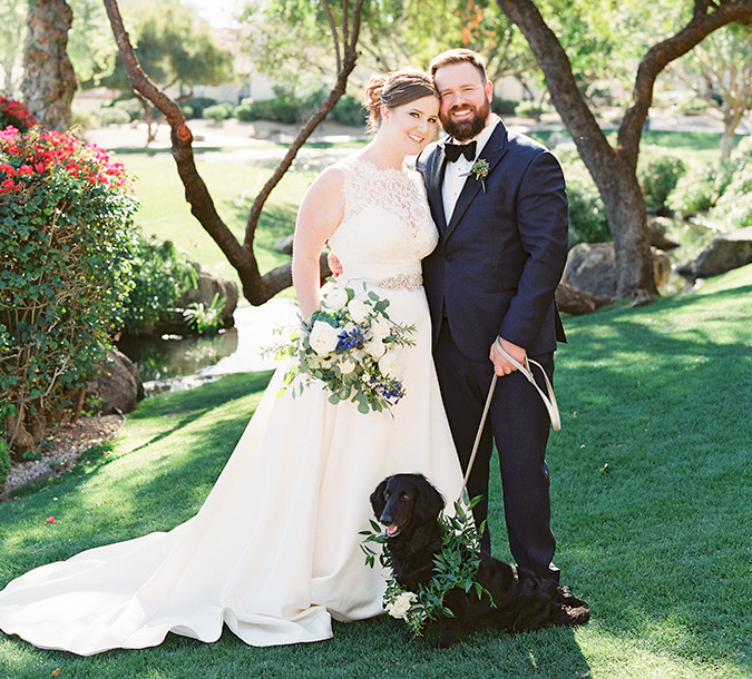 Smiling bride and groom with their dog outside during the day.