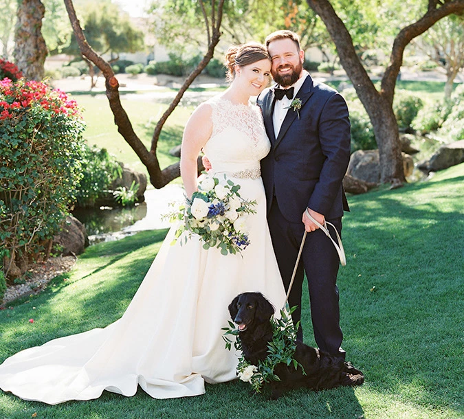 Smiling bride and groom with their dog outside during the day.