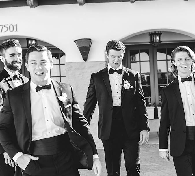 a black and white photo of a group of men in tuxedos walking from a building